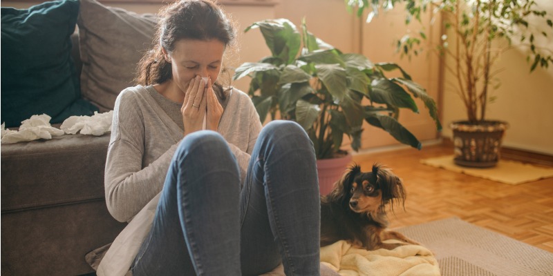 woman blowing her nose with her dog sitting next to her.